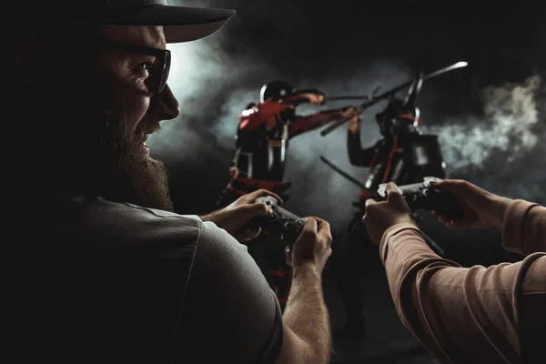Close-up shot of happy bearded man and woman playing samurai fighting in real life with gamepads on black — Stock Photo