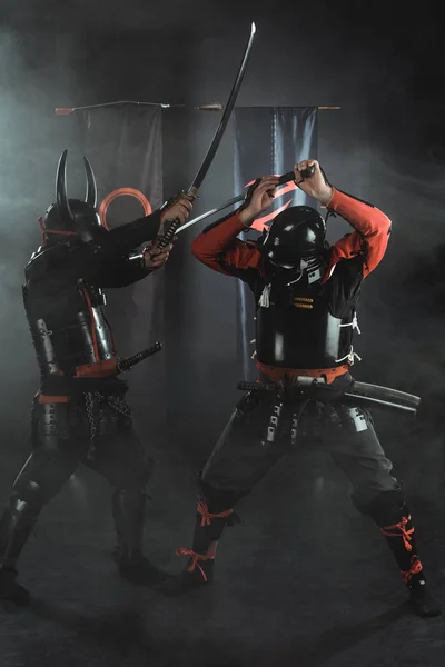 Samurai blindados tradicionales luchando con espadas sobre negro - foto de stock
