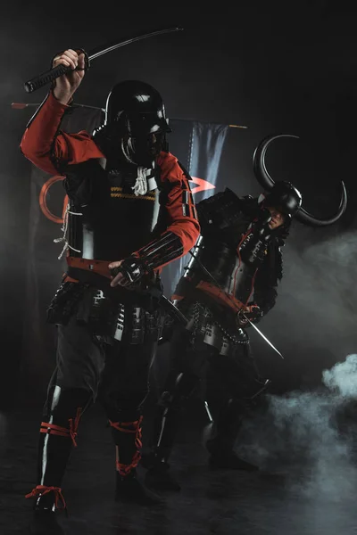 Armored samurai fighting with swords in front of clan symbols on flags on black — Stock Photo