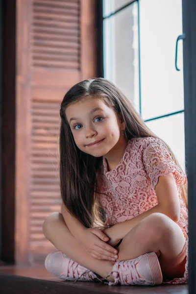Glückliches kleines Kind auf Fensterbank sitzend und in die Kamera blickend — Stockfoto