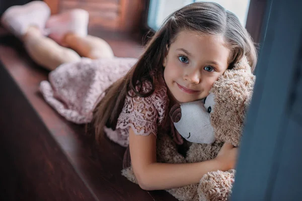 Kleines Kind umarmt Teddybär auf Fensterbank — Stockfoto