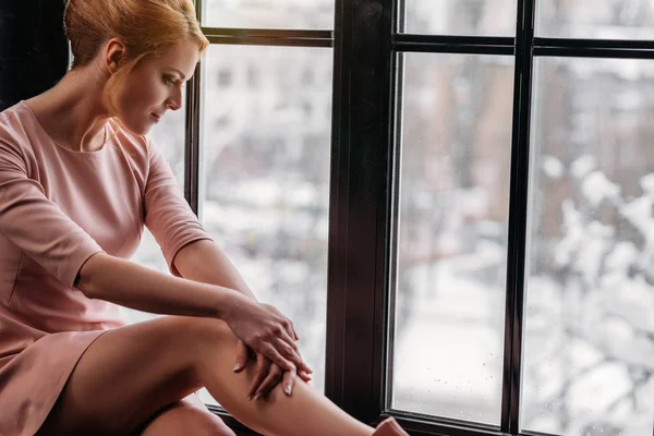 Nachdenkliche junge Frau in rosa Kleid sitzt auf Fensterbank und schaut nach unten — Stockfoto