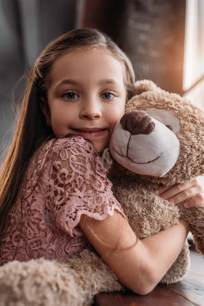 Heureux petit enfant embrassant ours en peluche ond regardant caméra — Photo de stock