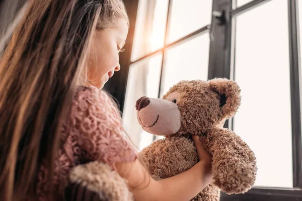 Adorable little child playing with teddy bear on windowsill — Stock Photo