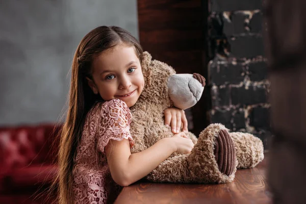 Lächelndes kleines Kind umarmt Teddybär auf Fensterbank in Dachgeschosswohnungen — Stockfoto