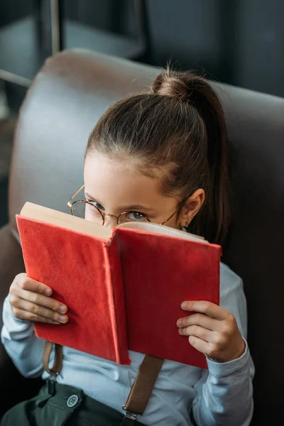 Close-up portrait of serious little child covering face with red book — Stock Photo