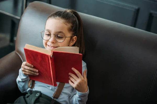 Happy little child reading book on couch at home — Stock Photo