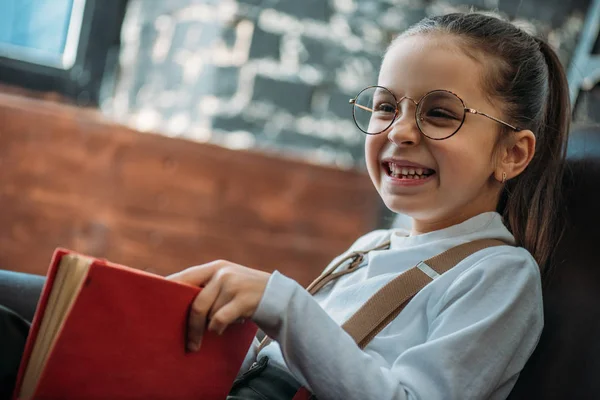 Criança pequena feliz leitura livro no sofá em casa — Fotografia de Stock