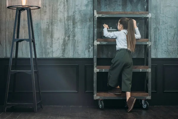 Rückansicht eines kleinen Kindes, das auf Bücherregalen in Loft-Wohnungen klettert — Stockfoto