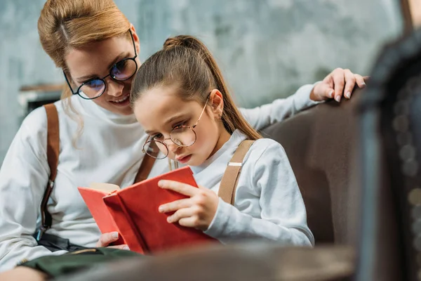 Young mother and daughter reading book together on couch — Stock Photo