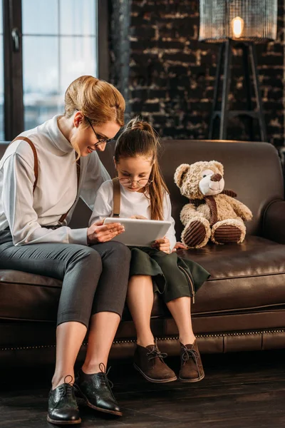 Madre e hija usando la tableta juntas en el sofá - foto de stock