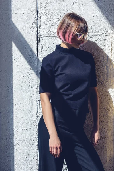 Vista lateral da menina da moda com o cabelo rosa inclinado na parede e olhando para baixo — Fotografia de Stock
