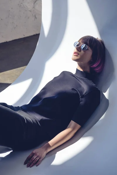 Menina elegante deitado em roupas pretas e óculos de sol — Fotografia de Stock