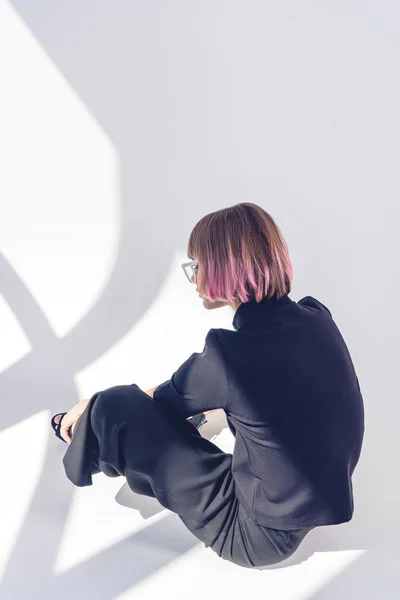Вид сзади стильной девушки, сидящей в черной одежде на белом — стоковое фото