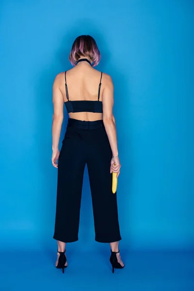 Вид сзади модной девушки, держащей банан на голубом — стоковое фото