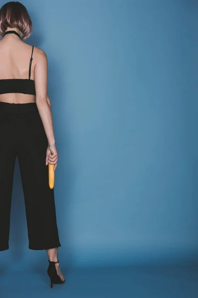 Back view of fashionable girl holding banana on blue — Stock Photo