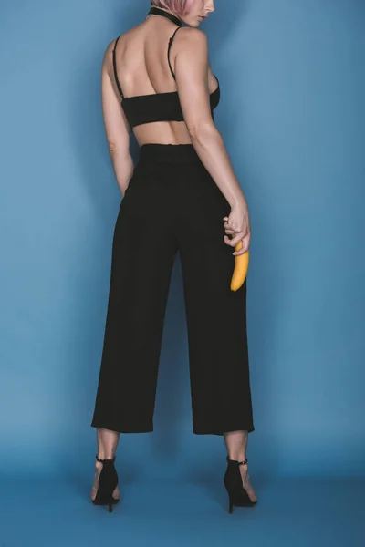 Vista trasera de chica elegante sosteniendo plátano en azul - foto de stock