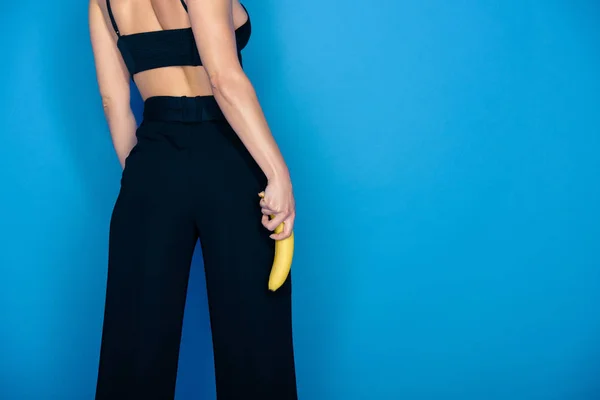 Imagen recortada de chica elegante sosteniendo plátano aislado en azul - foto de stock