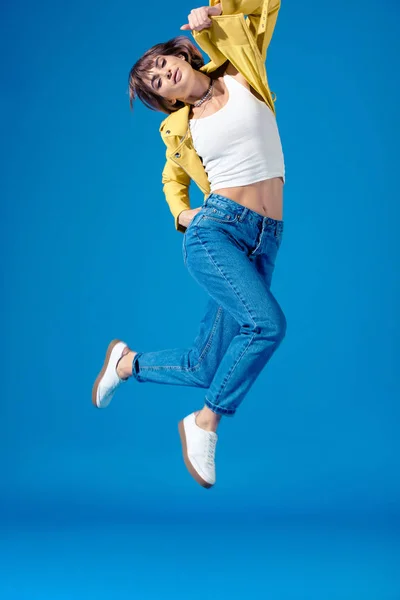 Девушка в стильной одежде прыжки изолированы на синий — стоковое фото