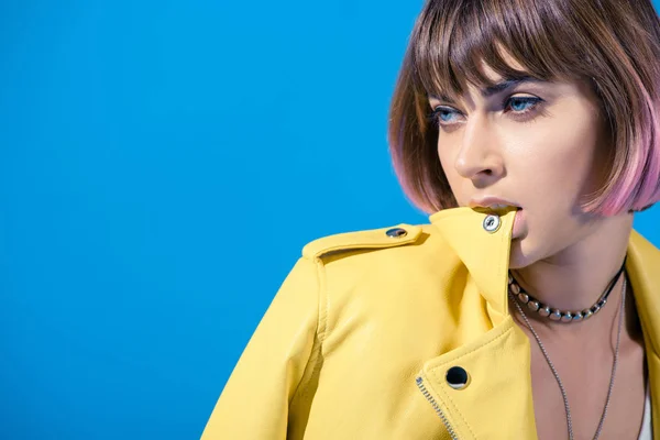 Porträt eines stilvollen Mädchens, das in eine Lederjacke beißt und isoliert auf blau wegschaut — Stockfoto