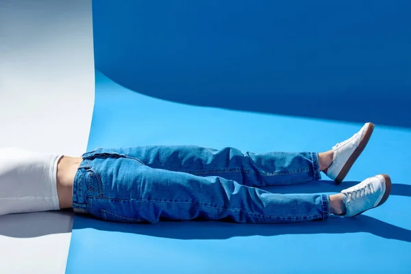 Imagem cortada de menina elegante deitado no chão branco e azul em jeans — Fotografia de Stock