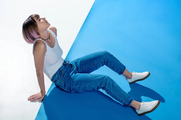 Chica elegante sentada en camisa y jeans en el piso blanco y azul - foto de stock
