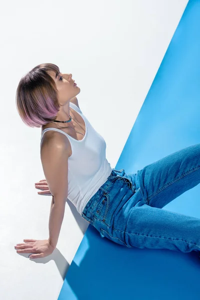 Fashionable girl sitting in shirt and jeans on white and blue floor — Stock Photo