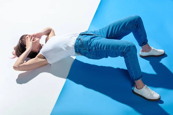 Chica de moda acostada en el suelo, cubriendo los ojos con las manos y haciendo levantamiento de caderas - foto de stock