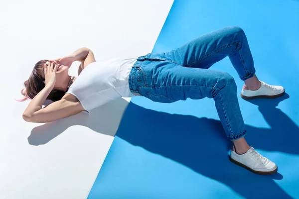 Fashionable girl lying on floor, covering eyes with hands and doing hips raise — Stock Photo