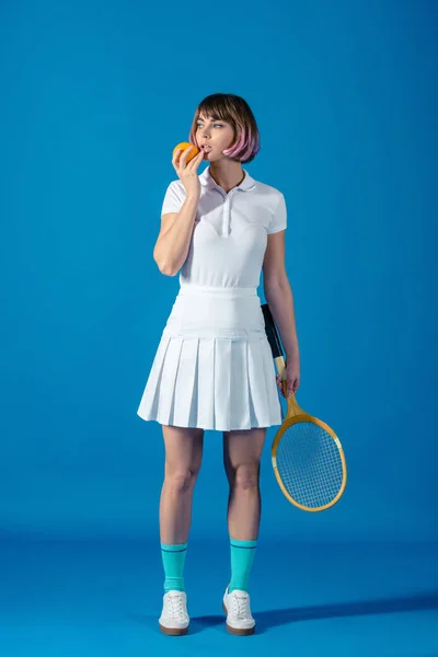 Тенісист стоїть з апельсином і тенісною ракеткою на синьому — стокове фото