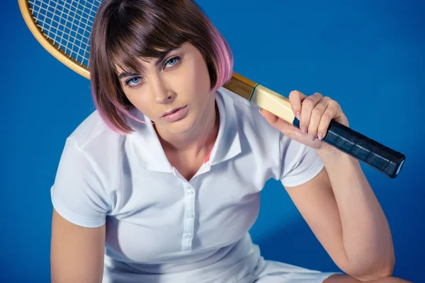 Жінка тенісистка з тенісною ракеткою дивиться на камеру ізольовано на синьому — стокове фото