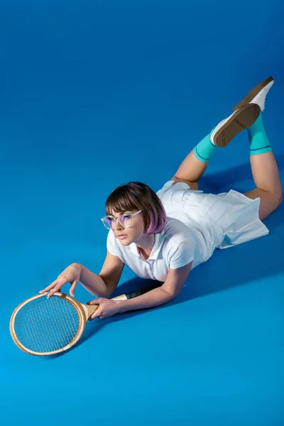 Verführerische Tennisspielerin auf Bauch liegend mit Tennisschläger auf blau — Stockfoto