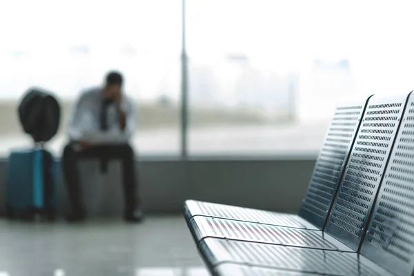 Nahaufnahme von Sitzen in der Flughafenlobby mit einem Geschäftsmann, der auf ein Flugzeug wartet, verschwommen auf dem Hintergrund — Stockfoto