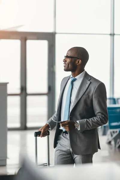 Hombre de negocios guapo con maleta caminando por el vestíbulo del aeropuerto - foto de stock