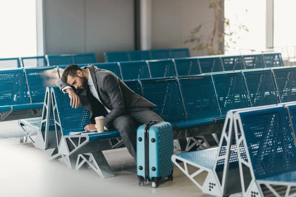 Soñoliento joven hombre de negocios esperando el vuelo en el vestíbulo del aeropuerto - foto de stock