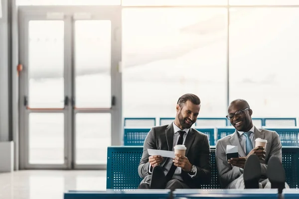 Colegas de negocios felices esperando el vuelo en el vestíbulo del aeropuerto - foto de stock