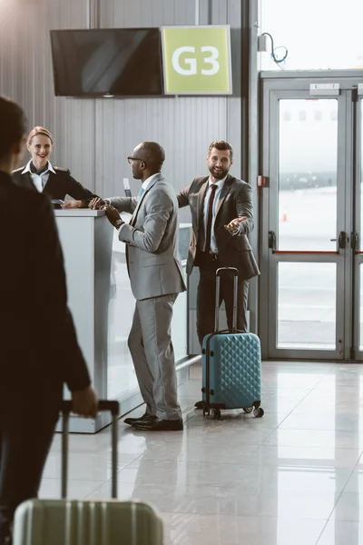 Businesspeople standing at airport reception to buy tickets while colleague walking to them — Stock Photo