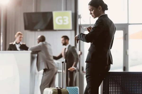 Hombre de negocios mirando el reloj mientras espera el vuelo en el vestíbulo del aeropuerto - foto de stock