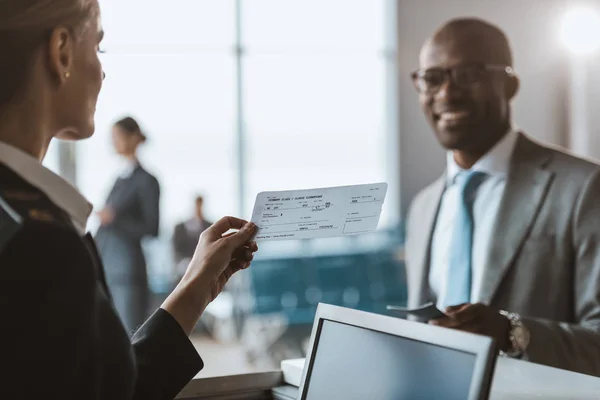 Gros plan d'un homme d'affaires afro-américain souriant qui remet un passeport au personnel du comptoir d'enregistrement de l'aéroport — Photo de stock