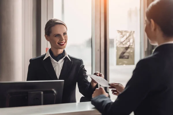 Junge Geschäftsfrau gibt Angestellten am Flughafen-Check-in-Schalter ein Ticket — Stockfoto