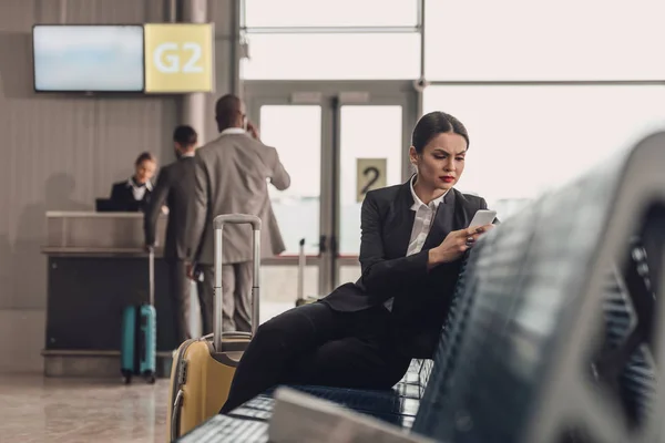 Joven mujer de negocios esperando avión en el vestíbulo del aeropuerto y el uso de teléfono inteligente - foto de stock