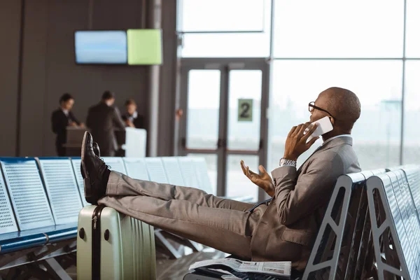 Hombre de negocios hablando por teléfono mientras espera el vuelo en el vestíbulo del aeropuerto - foto de stock