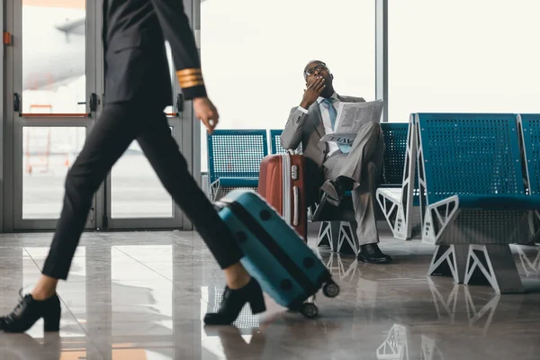 Homme d'affaires en attente d'un vol dans le hall de l'aéroport pendant que la femme pilote passe — Photo de stock