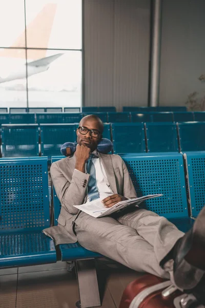 Aburrido hombre de negocios con almohada de viaje esperando el vuelo en el vestíbulo del aeropuerto - foto de stock