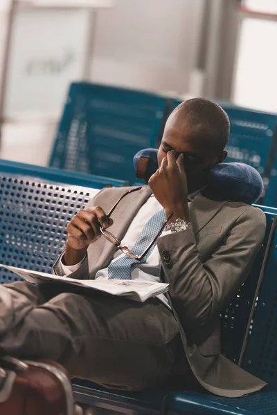 Сонний бізнесмен з подушкою для подорожей, яка чекає на політ у вестибюлі аеропорту — стокове фото