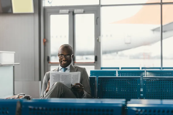 Guapo hombre de negocios leyendo el periódico mientras espera el vuelo en el vestíbulo del aeropuerto - foto de stock