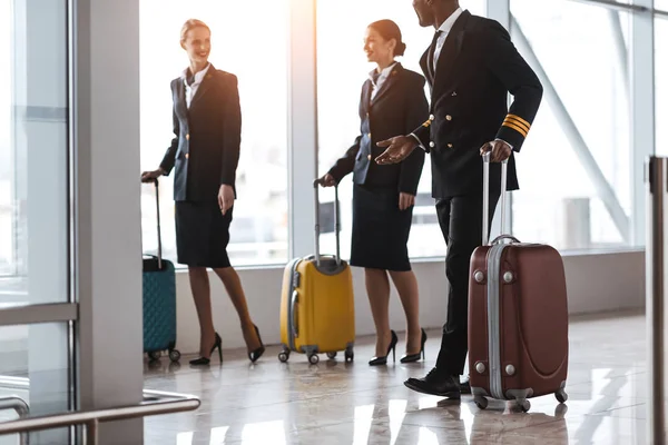 Pilot and stewardesses with luggage walking by airport — Stock Photo