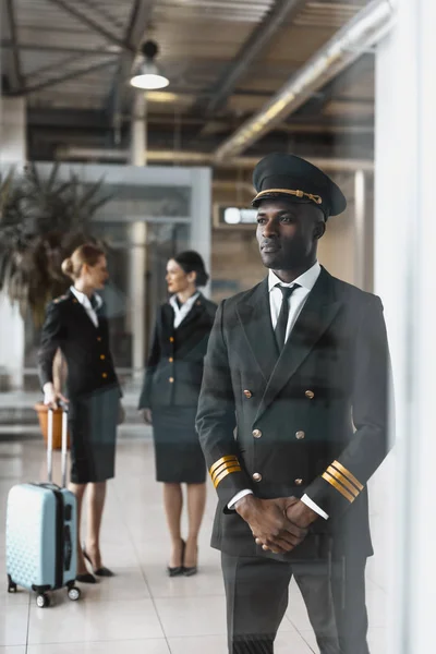 Handsome young pilot in airport with stewardesses before flight — Stock Photo