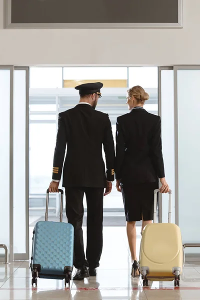 Rear view of pilot and stewardess walking by departure area — Stock Photo