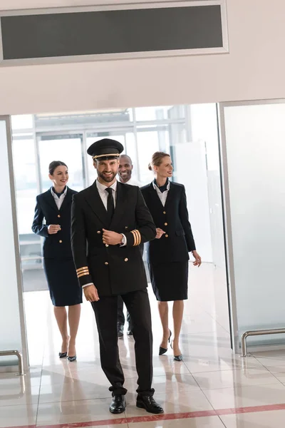 Beau jeune pilote marchant par l'aéroport avec son équipe — Photo de stock